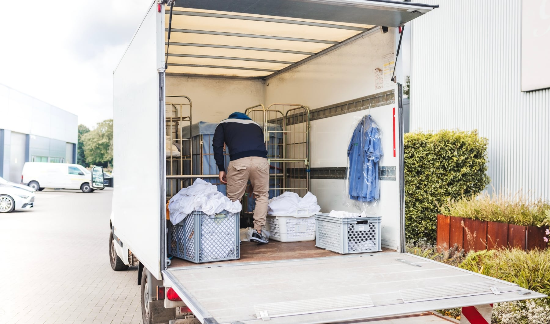 Chauffeur-livreur de blanchisserie industrielle manipulant des chariots de linge propre lors d’une livraison.