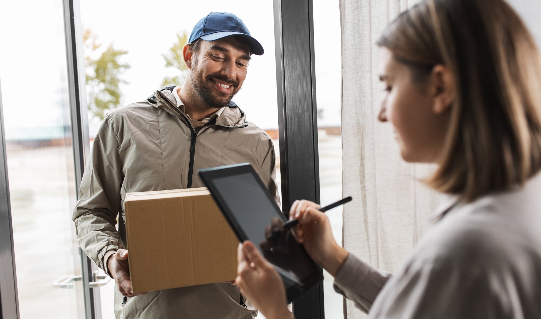 Livreur remettant un colis à un client pendant une livraison, avec signature d’un bon de réception sur ordinateur portable à domicile