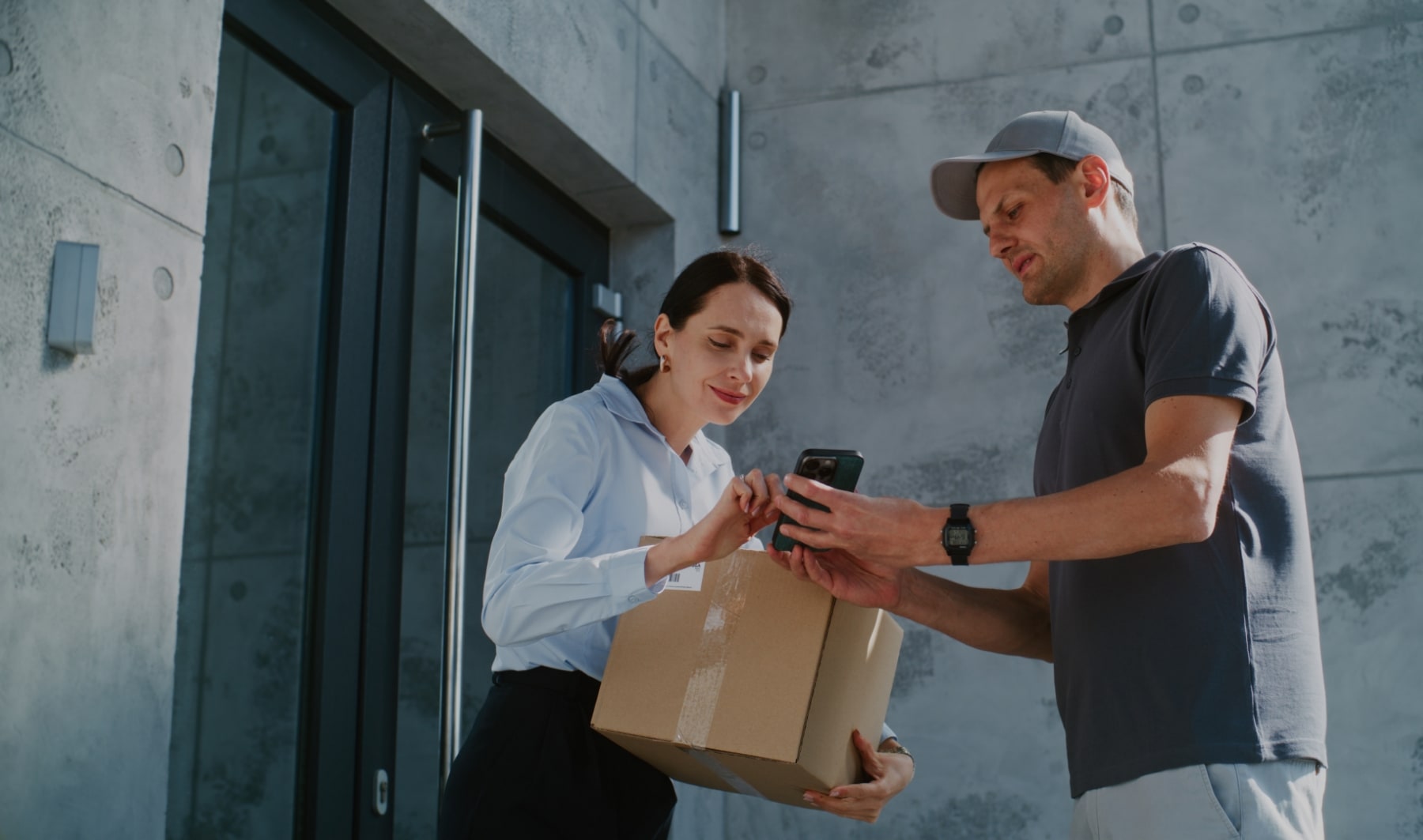 Livreur tenant un colis et présentant un smartphone à une cliente pour signer la réception du colis, illustrant une preuve de livraison électronique (ePOD).