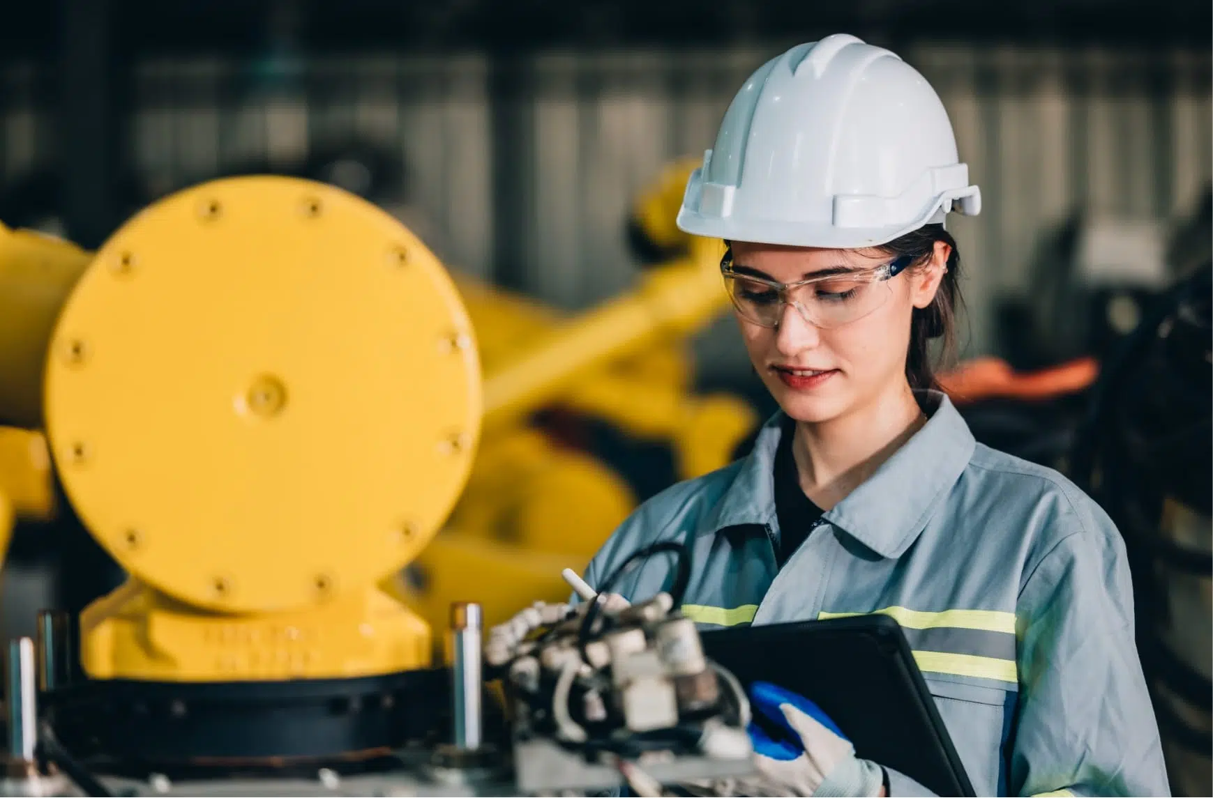 Eine Technikerin mit einem Tablet greift in eine Industriemaschine ein.