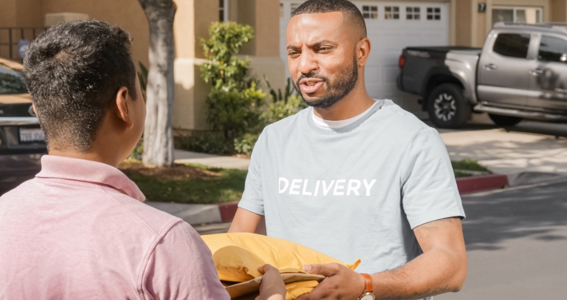 a smiling delivery man gives parcels to a person in the street