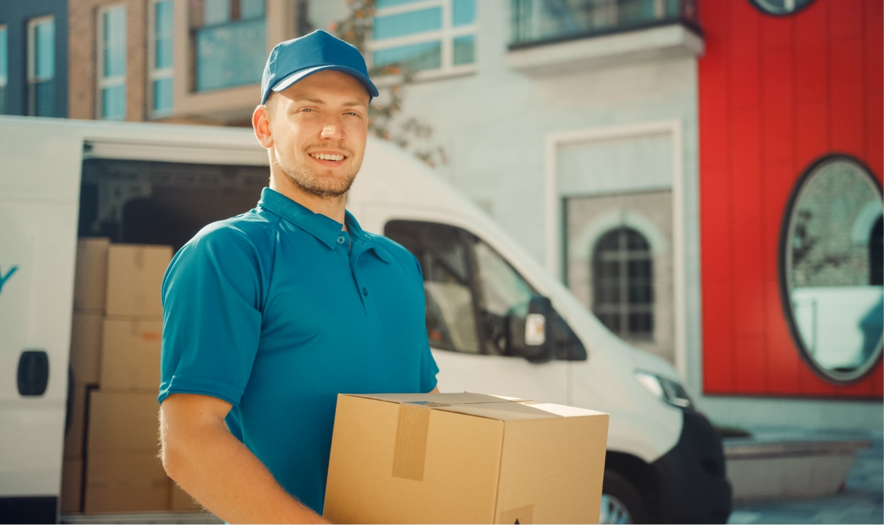 A smiling man with a parcel in his hands in front of a white van.