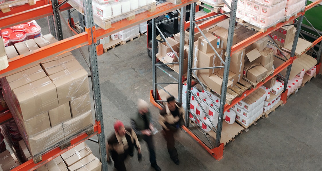 three people surrounded by parcels walking in a warehouse