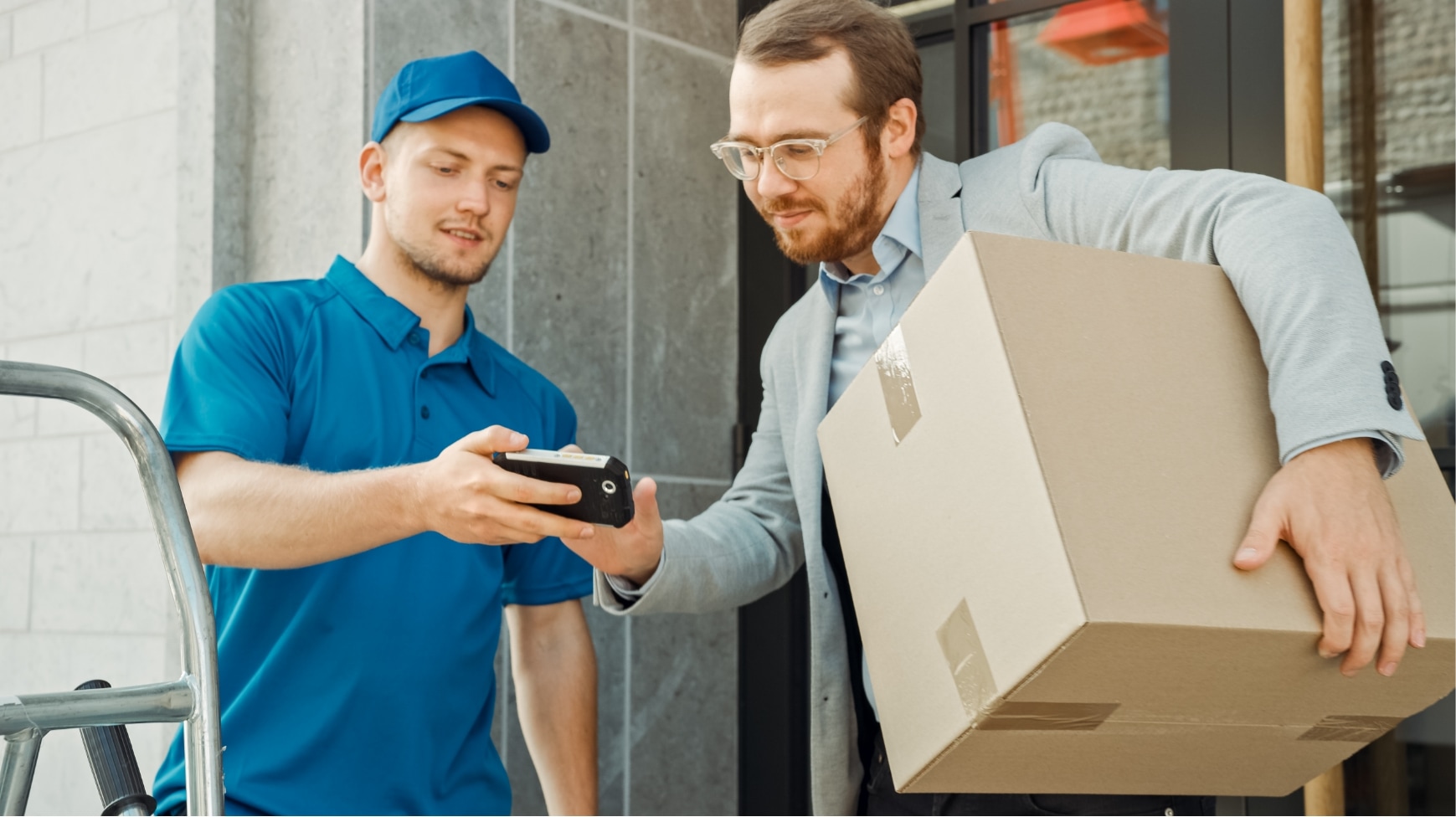A man with a parcel in his arms is signing on a deliveryman's smartphone.