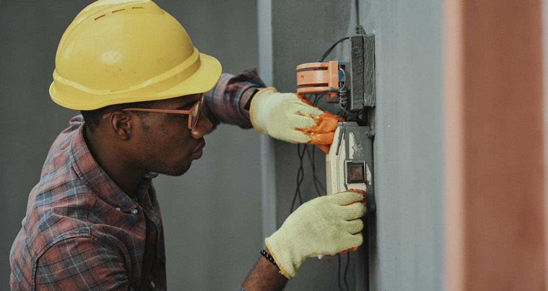 Techniker mit gelbem Helm bei Arbeiten an einem elektrischen Gerät